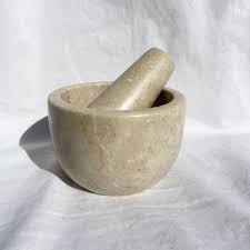 A light-colored stone mortar and pestle set placed on a white cloth background, with the pestle resting inside the bowl.