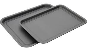 Two rectangular, non-stick metal baking trays are stacked at an angle on a white background.