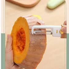 A hand is using a vegetable peeler to remove the skin from a thick slice of pumpkin.